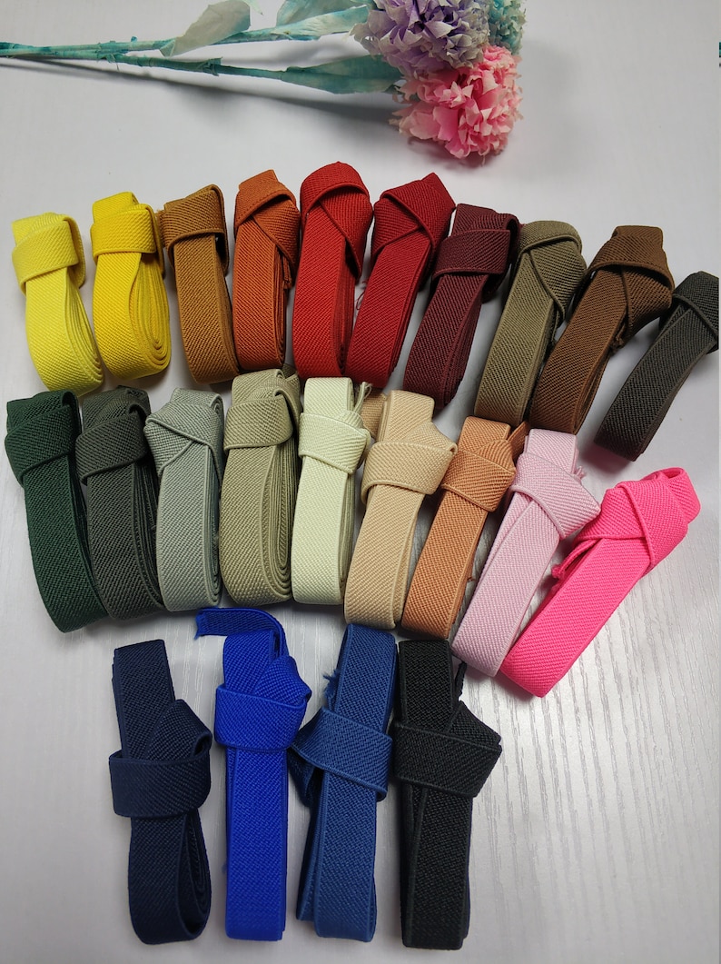 May include: Assortment of 18 elastic bands in various colors, including yellow, red, brown, green, beige, pink, blue, and black. The bands are folded in half and arranged in a row.