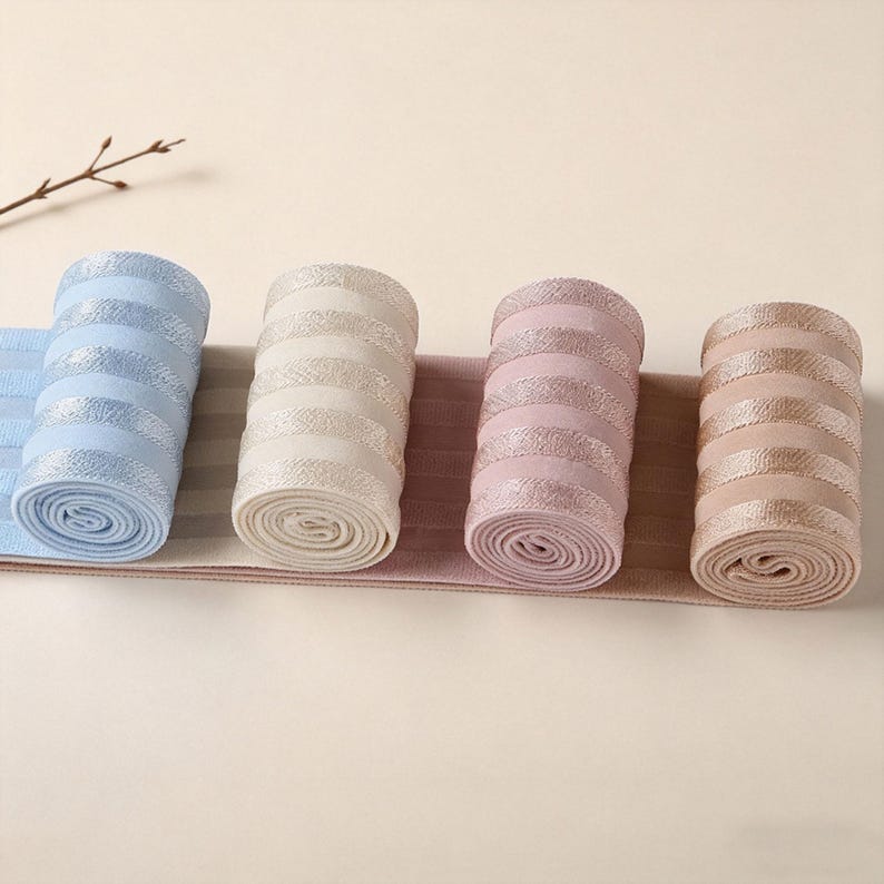 Peut inclure: Quatre rouleaux de bandes &eacute;lastiques en tissu c&ocirc;tel&eacute; dans les tons bleu clair, cr&egrave;me, vieux rose et beige. Chaque rouleau pr&eacute;sente un motif r&eacute;p&eacute;titif de rayures horizontales alternant entre mat et m&eacute;tallique brillant sur la surface textur&eacute;e.
