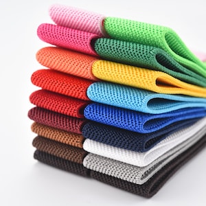 Puede incluir: Un conjunto de gomas elásticas de colores apiladas en varios colores, incluyendo rosa, verde, naranja, rojo, azul, marrón, blanco y negro.
