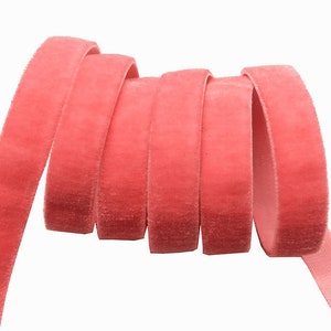 May include: A close-up of a spool of coral pink velvet ribbon. The ribbon is soft and plush, and it is perfect for adding a touch of elegance to any project.
