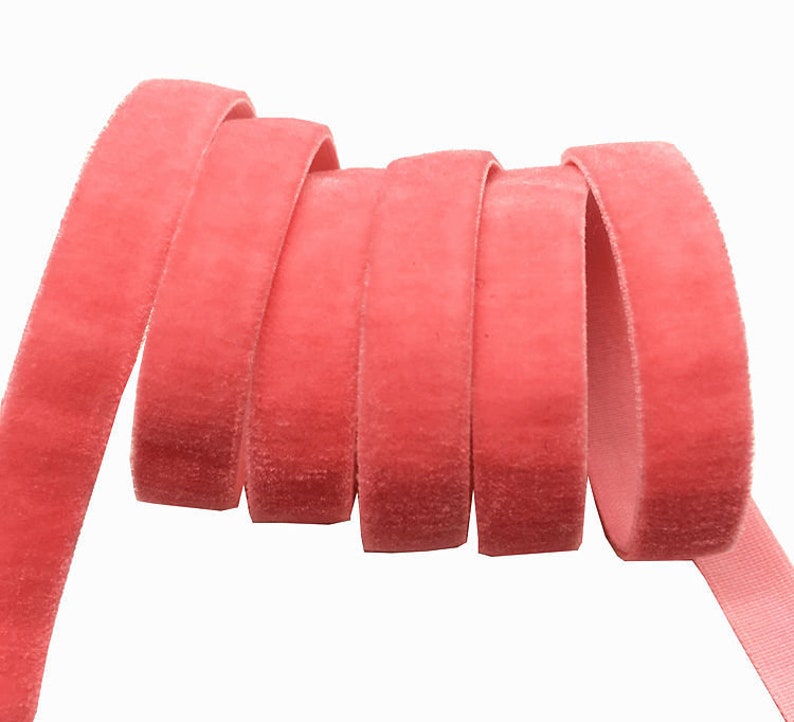 May include: A close-up of a spool of coral pink velvet ribbon. The ribbon is soft and plush, and it is perfect for adding a touch of elegance to any project.