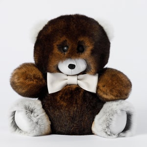 May include: A plush teddy bear with brown fur, white accents on the ears, paws, and a white bow tie. The bear has black button eyes and a white muzzle. The toy is sitting upright against a white background.