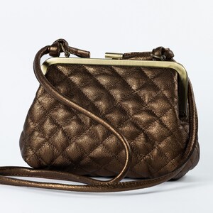 A brown quilted handbag with a gold clasp and a long strap, displayed against a white background.