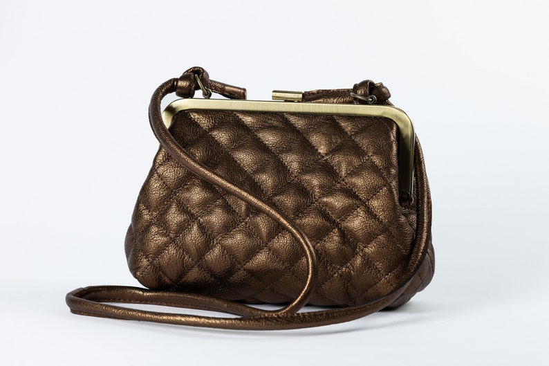 A brown quilted handbag with a gold clasp and a long strap, displayed against a white background.