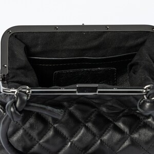 The interior view of a black quilted handbag, showing compartments and a clasp closure, against a white background.