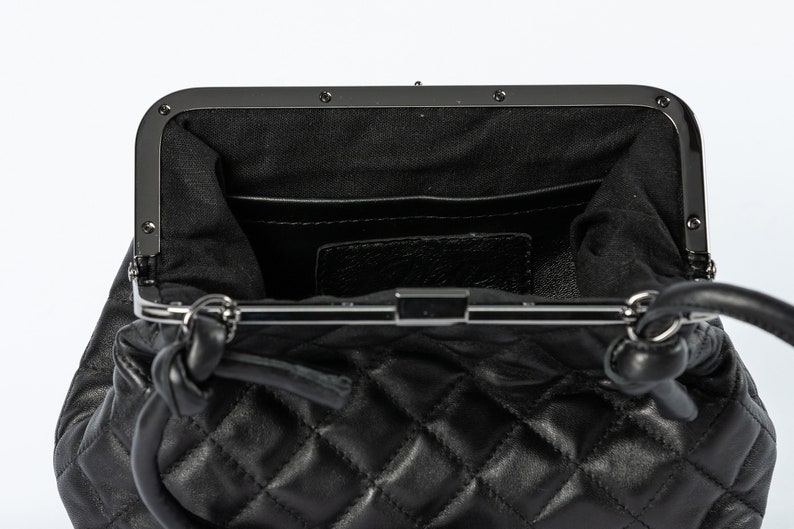 The interior view of a black quilted handbag, showing compartments and a clasp closure, against a white background.