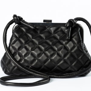 A black quilted handbag with a structured shape and a long strap, displayed against a white background.