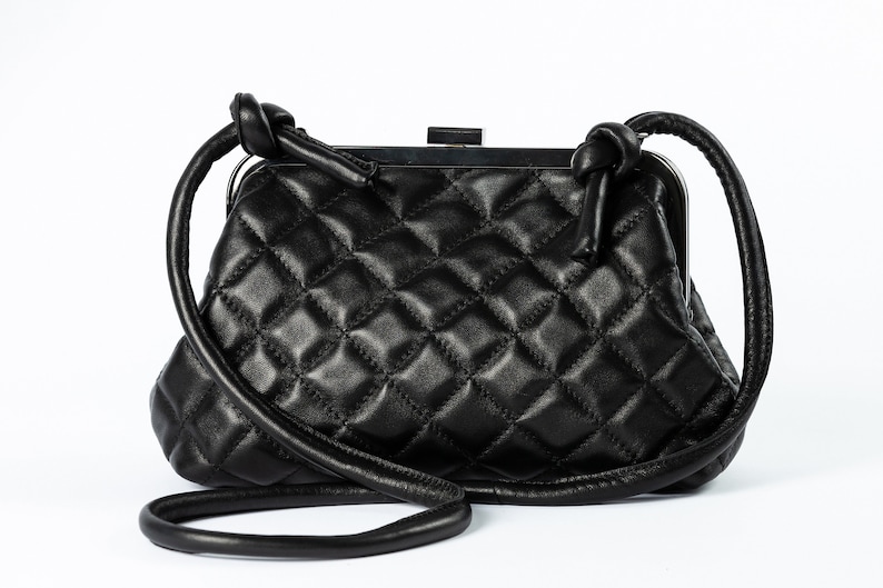 A black quilted handbag with a structured shape and a long strap, displayed against a white background.