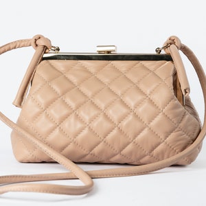 A beige quilted handbag with a vintage-style clasp and a detachable strap, displayed against a white background.