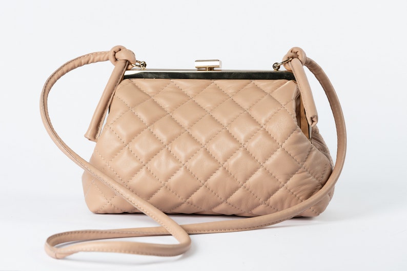 A beige quilted handbag with a vintage-style clasp and a detachable strap, displayed against a white background.