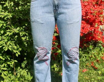 Könnte beinhalten: Hellblaue Jeans aus Denim mit roten Stickereien auf den Knien.