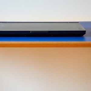 May include: A black laptop computer is closed and sitting on a blue surface with a wooden edge. A black computer mouse is on the surface to the right of the laptop.
