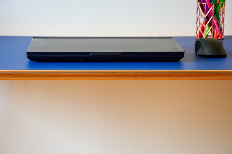 May include: A black laptop computer is closed and sitting on a blue surface with a wooden edge. A black computer mouse is on the surface to the right of the laptop.