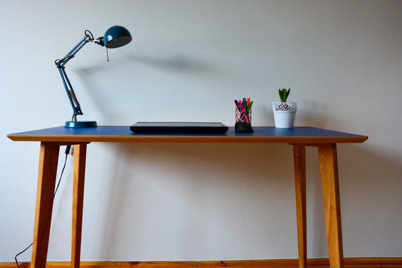 May include: A blue desk with a wooden frame and a blue lamp. A laptop, a cup of pens, and a potted plant are on the desk.