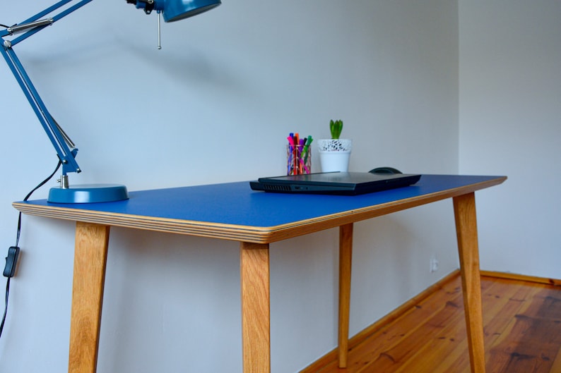 May include: A blue desk with a light wood frame and legs. The desk has a laptop, a potted plant, and a desk lamp on it.