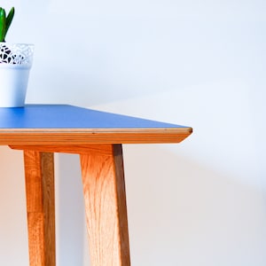 May include: A blue table with a wooden frame and legs. The table top is made of plywood and has a smooth, blue surface. The table is in a room with a white wall.