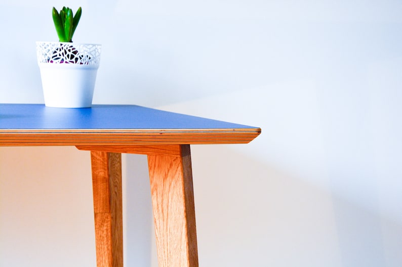 May include: A blue table with a wooden frame and legs. The table top is made of plywood and has a smooth, blue surface. The table is in a room with a white wall.