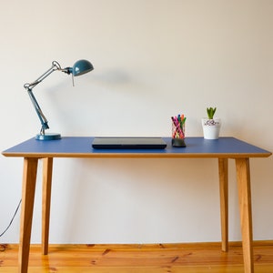 May include: A blue desk with a wooden frame and a black laptop on top. There is a desk lamp with a blue shade and a small potted plant on the desk.