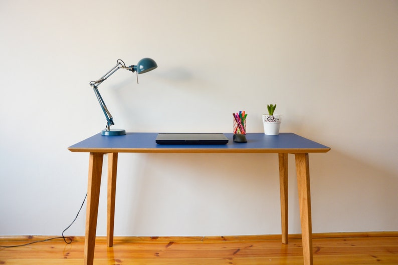 May include: A blue desk with a wooden frame and a black laptop on top. There is a desk lamp with a blue shade and a small potted plant on the desk.