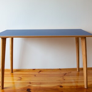 May include: A simple, modern desk with a blue tabletop and four wooden legs. The desk is made of wood and has a light wood finish.