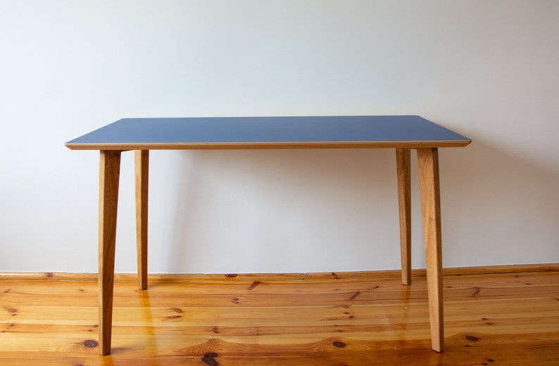May include: A simple, modern desk with a blue tabletop and four wooden legs. The desk is made of wood and has a light wood finish.