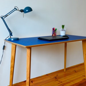 May include: A blue desk with a wooden frame and legs. A laptop, a small plant, and a blue desk lamp are on the desk.