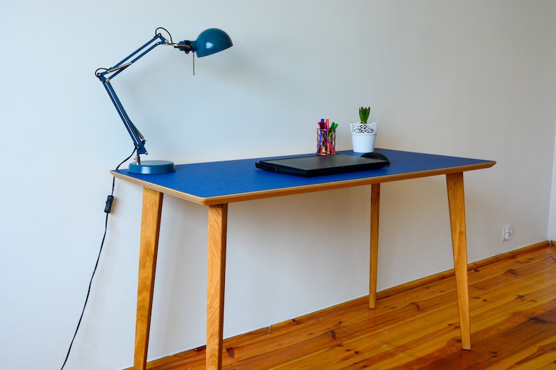 May include: A blue desk with a wooden frame and legs. A laptop, a small plant, and a blue desk lamp are on the desk.