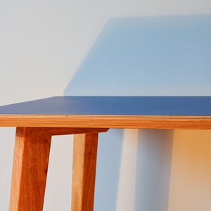May include: A blue and wood desk with a simple design. The desk has a blue top and wooden legs.