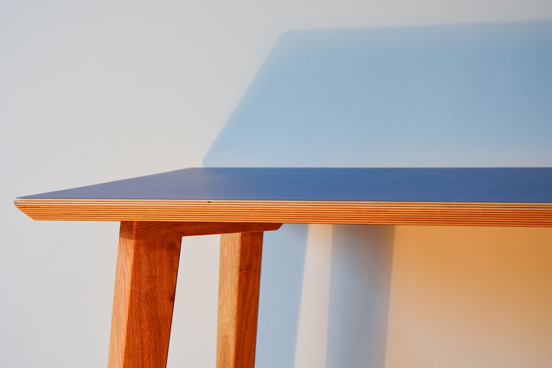 May include: A blue and wood desk with a simple design. The desk has a blue top and wooden legs.