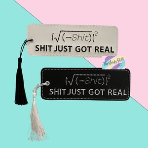 May include: Two black and white bookmark tassels with the text "√(-Shit))² SHIT JUST GOT REAL" on each. The bookmark tassels are on a pink and blue background.