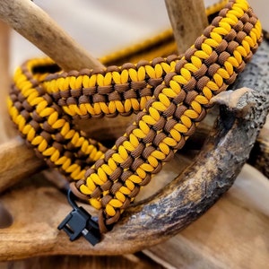 May include: A brown and yellow paracord bracelet with a black plastic clasp. The bracelet is wrapped around a set of antlers.