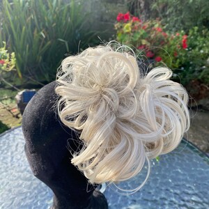 May include: A blonde hairpiece in a messy bun style. The hairpiece is on a black mannequin head.