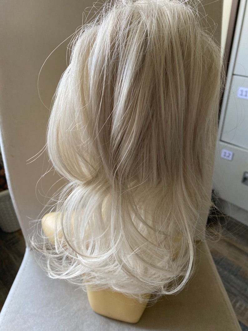 May include: A long, white blonde hair extension for adding volume and length to a ponytail.