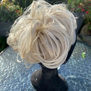 May include: A blonde hair bun extension on a black mannequin head. The hair is styled in a messy bun.