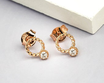 Könnte beinhalten: Ein Paar goldfarbene Ohrringe mit einem kleinen, klaren Edelstein in der Mitte jedes Ohrrings. Die Ohrringe haben ein verdrehtes Seil-Design, das einen Kreis bildet.