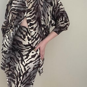 May include: A brown and white zebra print blouse and skirt set. The blouse has a long sleeve and a button-up front. The skirt is midi length and has a fitted silhouette.