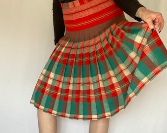 May include: A pleated skirt with a plaid pattern in red, green, brown, and white. The skirt has a high waist and is made of a thick fabric.