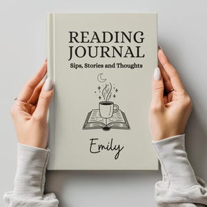 May include: A cream-colored reading journal held by hands. The cover reads "READING JOURNAL" above "Sips, Stories and Thoughts." A coffee cup and book graphic is below the text, with the name "Emily" at the bottom.