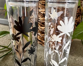 May include: Two clear plastic tumblers with floral designs. One tumbler has black floral designs and the other has white floral designs.
