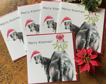 Könnte beinhalten: Weihnachtskarten mit rotem Rand, die einen Windhund mit Weihnachtsmütze und kariertem Kragen zeigen. Die Karten tragen den Text "Merry Kissmas!". Ein roter Weihnachtsstern und Stechpalmenzweige sind im Hintergrund.