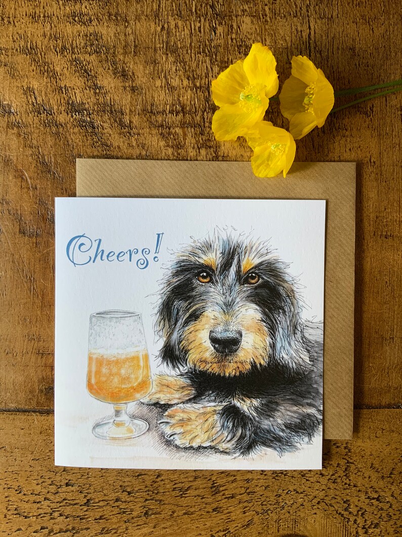 May include: A greeting card featuring a black and tan dog with a glass of beer. The card says "Cheers!" in blue lettering.