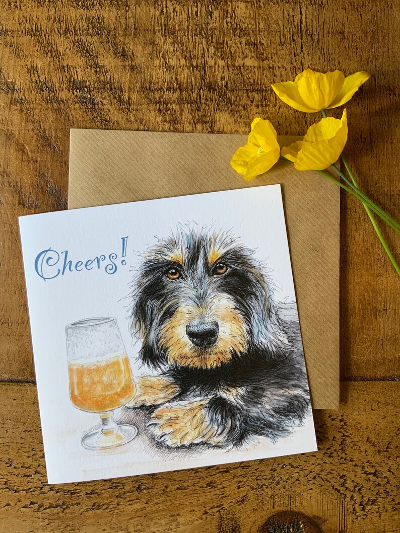 May include: A greeting card with a black and brown dog with a glass of beer. The card says "Cheers!" in blue text.