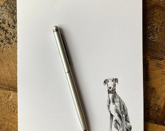 Puede incluir: Un bloc de notas blanco con la palabra "Notes" impresa en la parte superior. Un bolígrafo plateado está sobre el bloc de notas. Una ilustración en blanco y negro de un perro está en la parte inferior del bloc de notas.