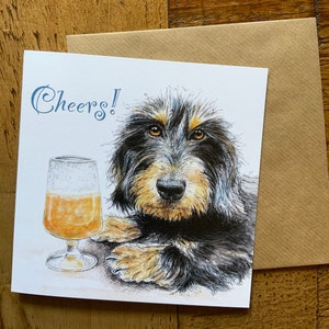 May include: A greeting card with a black and brown dog with a glass of beer. The card says "Cheers!" in blue text.