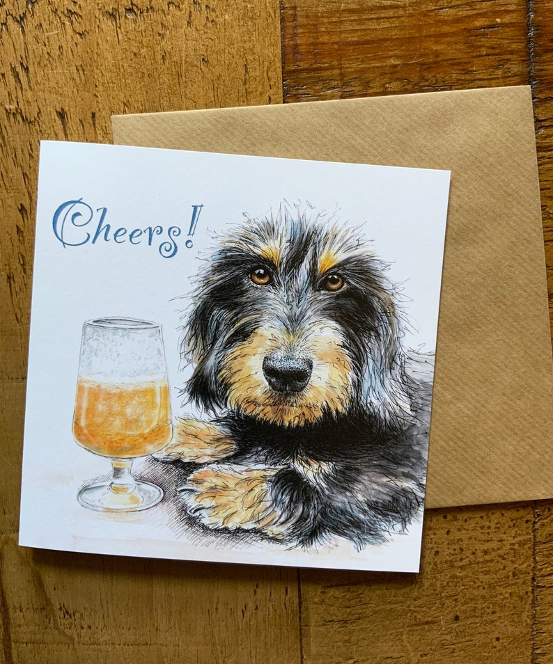 May include: A greeting card with a black and brown dog with a glass of beer. The card says "Cheers!" in blue text.