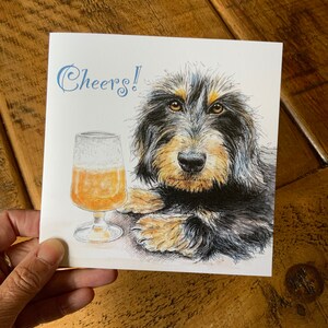 May include: A greeting card with a black and brown dog with a glass of beer. The card says "Cheers!" in blue cursive.