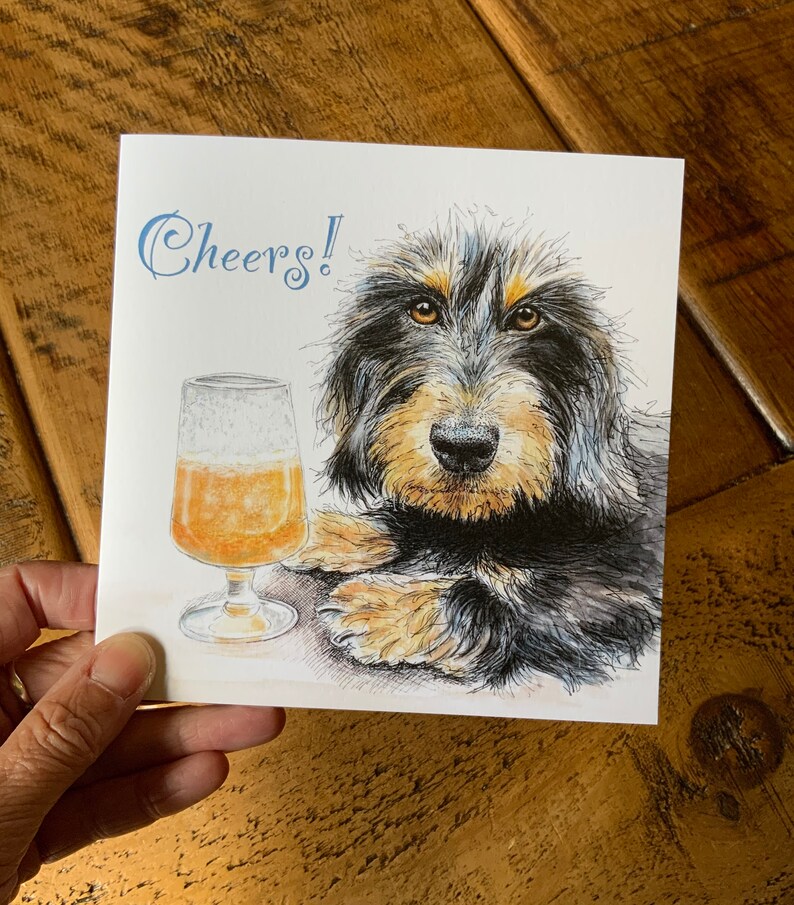 May include: A greeting card with a black and brown dog with a glass of beer. The card says "Cheers!" in blue cursive.