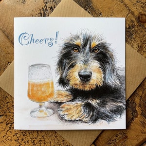 May include: A greeting card with a black and tan dog with a glass of beer. The card says "Cheers!" in blue lettering.