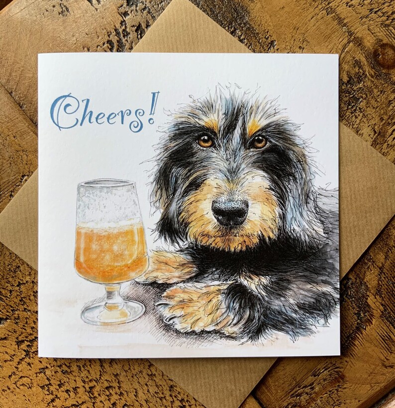 May include: A greeting card with a black and tan dog with a glass of beer. The card says "Cheers!" in blue lettering.