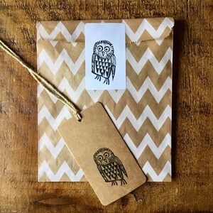 May include: A brown paper bag with a white zig-zag pattern, a white rectangular sticker, and a brown tag. Each features a black and white owl illustration. A natural twine string is attached to the tag.